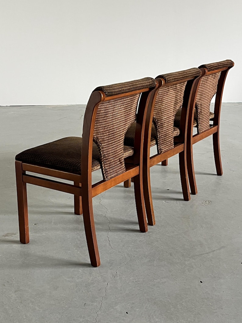 May include: Three wooden chairs with brown woven backs and seats. The chairs have a curved back design and are made of a light-colored wood. The woven material on the backs and seats is a darker brown color, creating a contrast.
