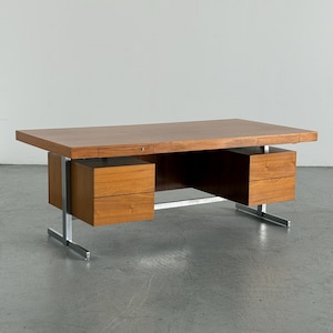 Puede incluir: Un escritorio rectangular de madera con una superficie plana, dos cajones integrados y dos unidades de pedestal separadas, cada una con dos cajones. El escritorio está sostenido por una estructura de metal plateado con patas en forma de T.