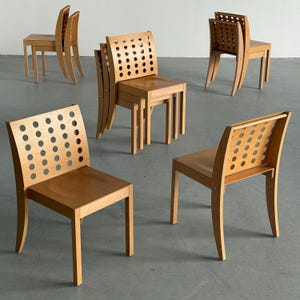 May include: Several wooden chairs with light brown finishes are arranged in a room. Some chairs have backs with circular cutouts, while others have solid backs. The chairs have a modern design and are suitable for various interior settings.