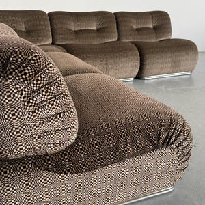 May include: A modular brown sofa with a geometric patterned seat cushion and backrest. The sofa has a low profile with rounded cushions and a silver metal base. The fabric has a textured appearance.