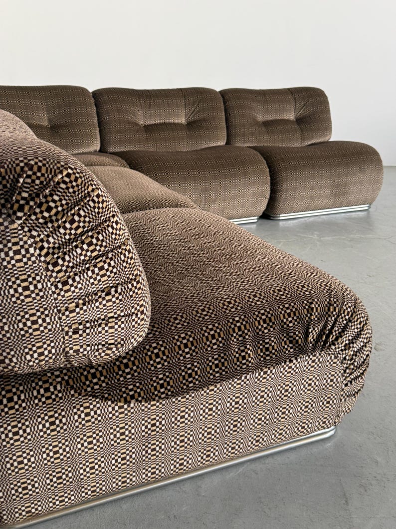 May include: A modular brown sofa with a geometric patterned seat cushion and backrest. The sofa has a low profile with rounded cushions and a silver metal base. The fabric has a textured appearance.