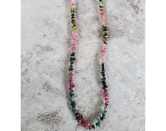 May include: A long necklace made of small, irregular, multi-colored gemstone chips. The chips are shades of pink, green, and black.