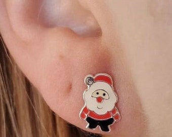 May include: A pair of silver stud earrings featuring a cartoon Santa Claus design with a red hat, white beard, and black boots. The Santa Claus has a red and white suit and a small clear rhinestone on his hat.