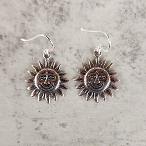 May include: A pair of silver earrings featuring a smiling sun design.