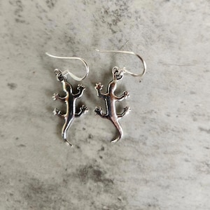 May include: A pair of silver lizard earrings with a dangling design.