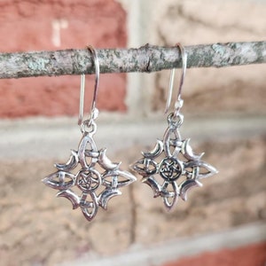May include: A pair of silver earrings with a Celtic knot design. The earrings are hanging from a branch.