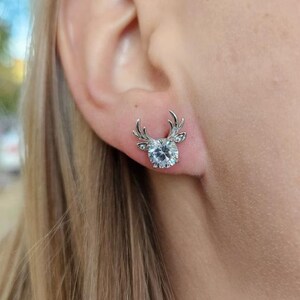 May include: A pair of silver earrings with a clear crystal in the center and a deer antler design.