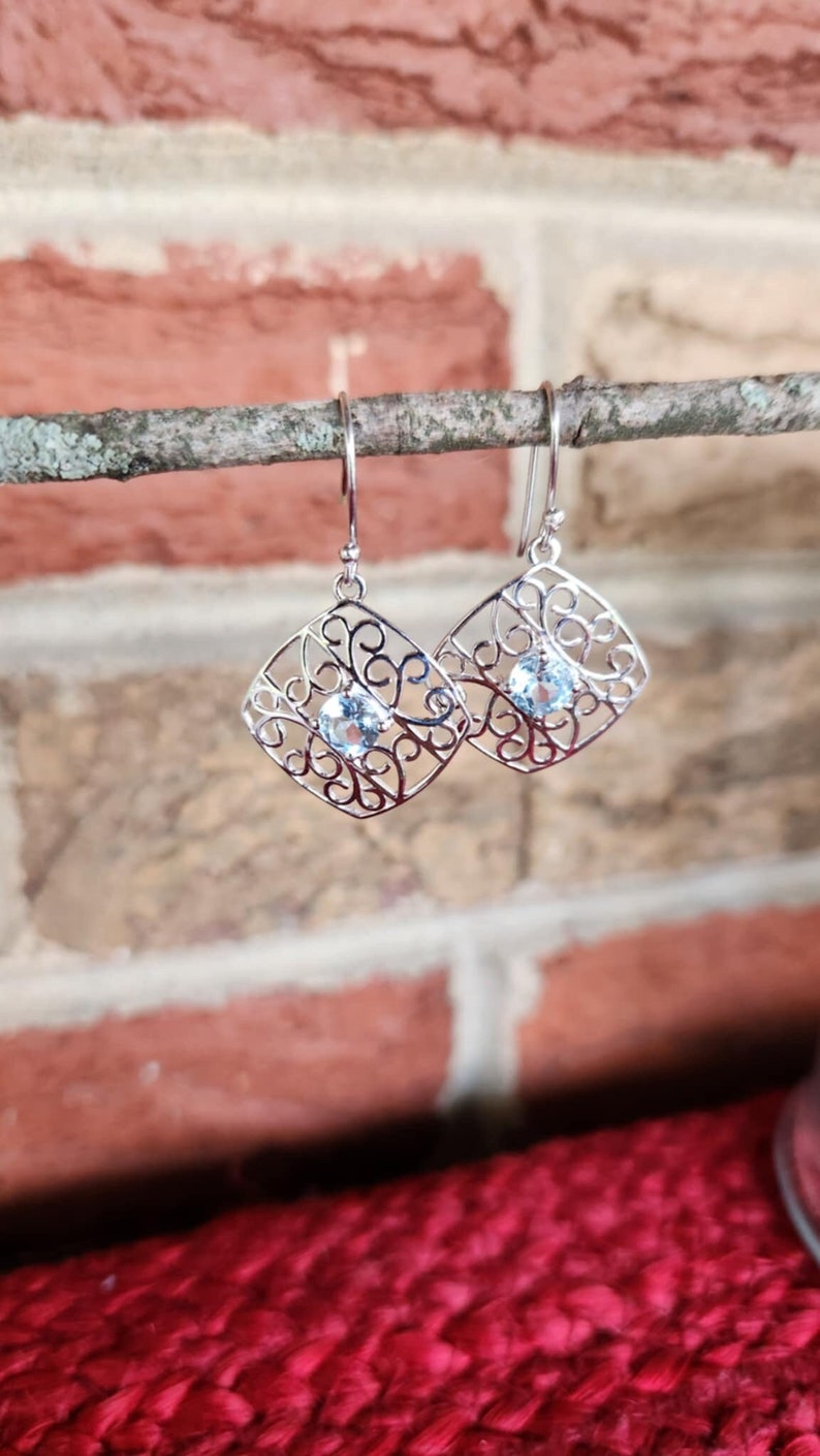 May include: Silver filigree earrings with a light blue gemstone in the centre of each earring.