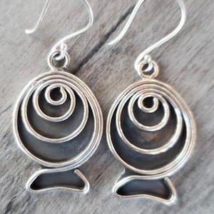 May include: A pair of silver earrings with a circular design featuring concentric circles. The earrings have a hook closure.