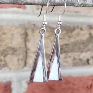 May include: Silver-tone dangle earrings with a triangular design. Each earring features a white, opal-like inlay within a silver frame. The earrings hang from simple silver hooks, showcasing a minimalist and geometric aesthetic.
