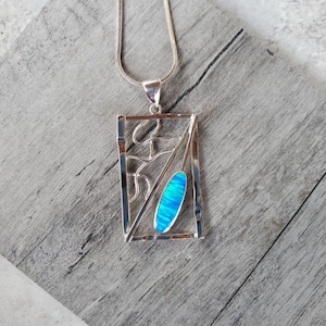 May include: A silver necklace with a rectangular pendant featuring a blue opal stone set in a geometric design.