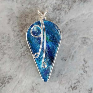 May include: A teardrop-shaped pendant with a vibrant blue and green glass center, encased in a silver-colored metal frame. The pendant features a decorative silver wire design. The jewelry is suitable for everyday wear.