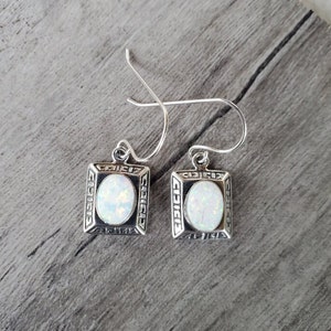 May include: A pair of silver earrings with white opal stones set in a square frame with a Greek key design.