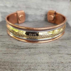 May include: A copper magnetic bracelet with a gold band and a patterned design. The bracelet has two magnetic clasps.