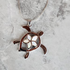 May include: A silver necklace with a white opal flower pendant in the shape of a turtle.