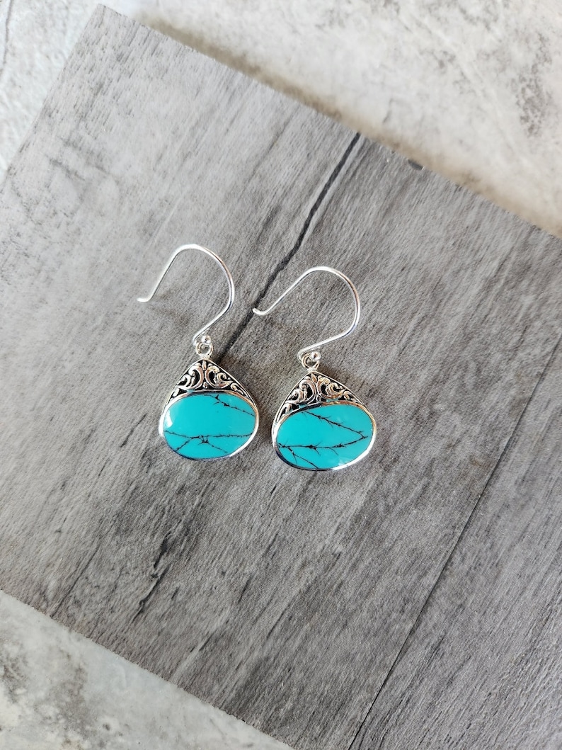 Puede incluir: Un par de pendientes de plata con piedras turquesa. Las piedras son de forma ovalada y tienen un color azul y verde.