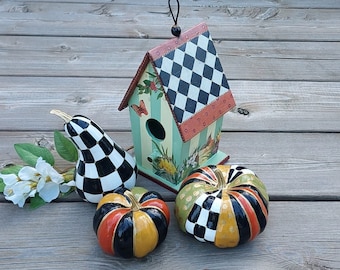 Peut inclure: Une maisonnette en bois peinte avec un toit à damiers, un corps rayé vert et blanc et des détails floraux. Trois gourdes sont peintes en damier noir et blanc, noir et or, et noir, or et rouge.