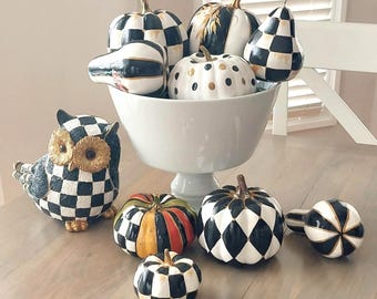 Peut inclure: Une collection d'objets décoratifs comprenant une figurine de hibou à damier noir et blanc et diverses courges et citrouilles dans un bol sur pied blanc. Les objets présentent des motifs à damier, à pois et arlequin avec des accents dorés.