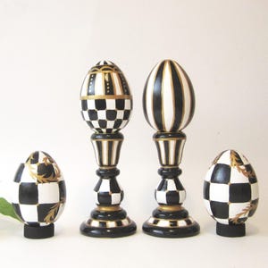 May include: Two decorative egg-shaped ornaments on pedestals and two smaller egg-shaped ornaments on circular bases. All items feature a black and white checkered or striped pattern with gold painted accents and details throughout the set.