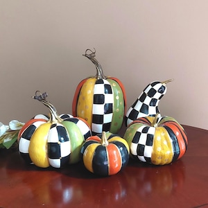May include: A collection of four decorative pumpkins and one gourd featuring a hand-painted pattern of black and white checks, solid orange, yellow, and green segments, and gold polka dots. Each piece has a metallic gold stem and textured finish.