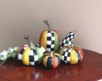 May include: A collection of four decorative pumpkins and one gourd featuring a hand-painted pattern of black and white checks, solid orange, yellow, and green segments, and gold polka dots. Each piece has a metallic gold stem and textured finish.