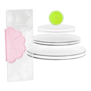 May include: A set of four clear acrylic cake circles with a pink silicone cake scraper. The scraper has the text "Lacupella Italia" on it. The cake circles are stacked on top of each other. A green circle with a bullseye design is on top of the stack.