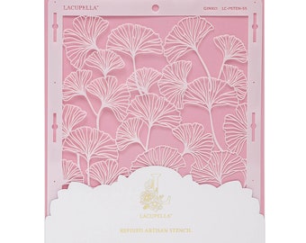 May include: Pink plastic stencil with a white design of ginkgo leaves. The stencil is labeled "GINKO LC-JSTEN-55" and "LACUPPELLA" with the text "REFINED ARTISAN STENCIL. www.lacupelladesign.com"