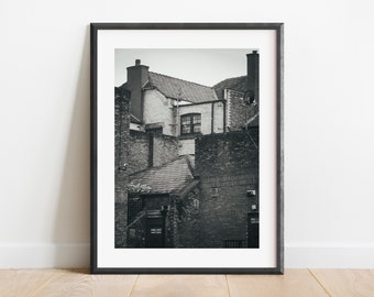 May include: Black and white photograph of a brick building with a fire escape. The building has a flat roof and a single window. The fire escape is made of metal and has a ladder leading up to it.