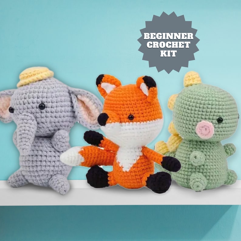 Op de afbeelding: Een beginnershaakpakket met drie gehaakte knuffels: een grijze olifant, een oranje vos en een groene dinosaurus. Het pakket is gelabeld met "Beginnershaakpakket".