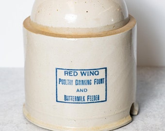 May include: A white ceramic poultry drinking fount and buttermilk feeder with blue lettering that reads "Red Wing Poultry Drinking Fount and Buttermilk Feeder".