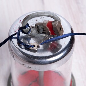 May include: A silver and glass piggy bank with a red interior. The lid is secured with a small padlock and a blue ribbon. A key is attached to the padlock.