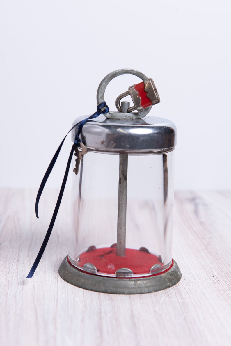 May include: A vintage glass jar with a metal lid and a red padlock. The jar has a metal rod running through the center and a red base. A blue ribbon is tied around the lid with two keys attached.