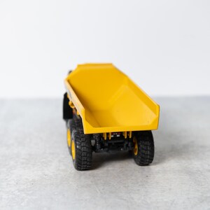 May include: A yellow toy dump truck with black wheels. The truck bed is raised and empty.