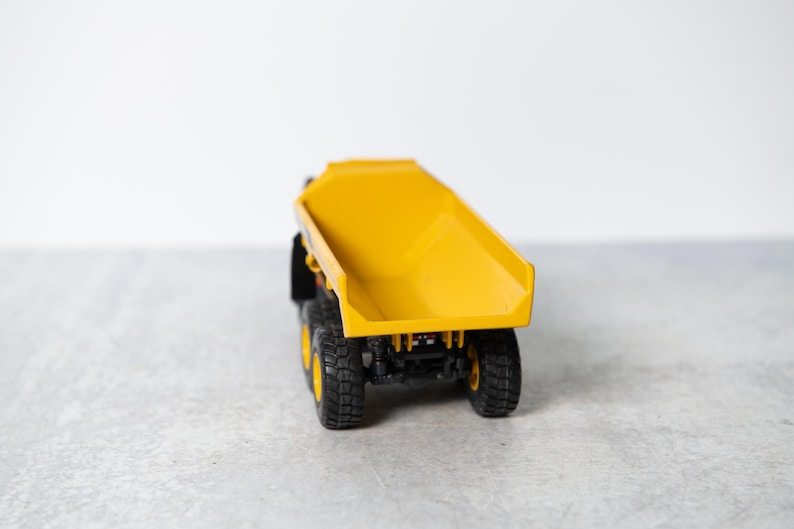 May include: A yellow toy dump truck with black wheels. The truck bed is raised and empty.