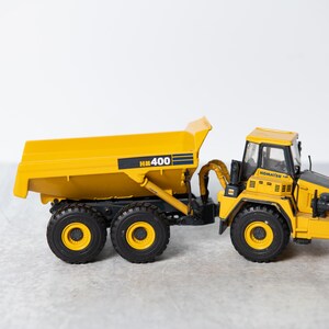 May include: A yellow toy dump truck with a black cab and the text "HM 400" on the side. The truck has four black wheels and a black metal frame.