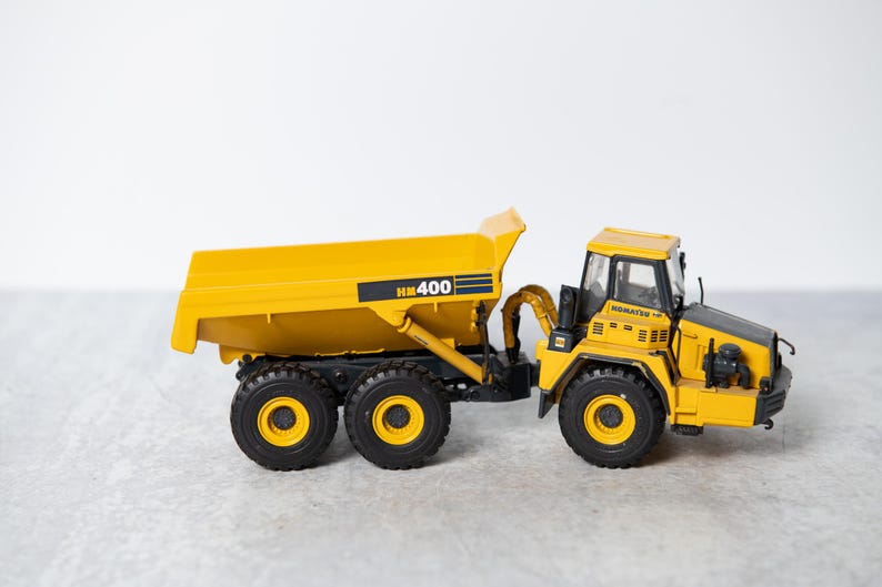 May include: A yellow toy dump truck with a black cab and the text "HM 400" on the side. The truck has four black wheels and a black metal frame.