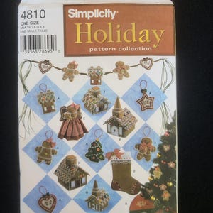 Könnte beinhalten: Simplicity Holiday Schnittmuster-Kollektion Box mit verschiedenen Weihnachtsornament-Designs. Die Box zeigt Lebkuchenmänner, Häuser, einen Strumpf und einen Weihnachtsbaum. Die Box ist mit "4810 ONE SIZE" beschriftet.