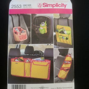 May include: Simplicity pattern 2553 for car organizers. The pattern features various designs, including seat-back organizers and console storage. The image shows examples of the finished products in yellow, pink, and green, with multiple pockets and compartments.