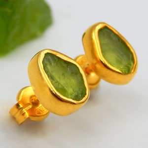 May include: A pair of gold earrings with green gemstone settings. The gemstones are irregularly shaped and have a rough, natural look.