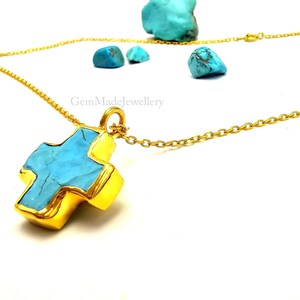 May include: A gold chain necklace with a turquoise cross pendant. The cross is made of gold and has a turquoise stone in the center. The chain is a delicate, cable chain.