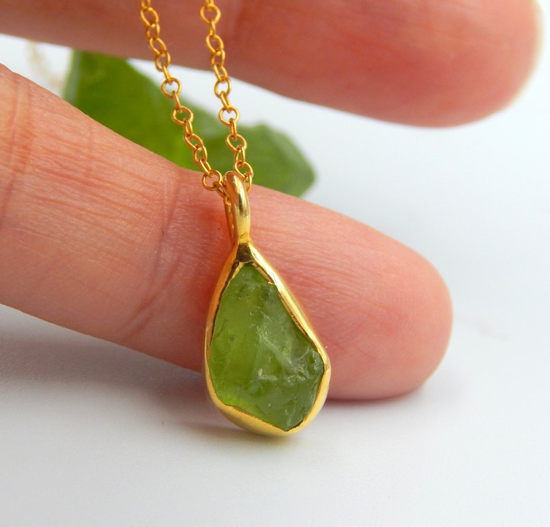 May include: A gold chain necklace with a green peridot pendant. The peridot is a raw, uncut stone with a natural, irregular shape.