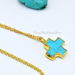 May include: A gold chain necklace with a turquoise cross pendant. The cross is set in gold and has a turquoise stone in the center. GemMadeJewellery is printed on the image.