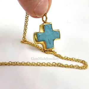 May include: A gold chain necklace with a turquoise cross pendant. The cross is a simple, geometric design with a slightly textured surface.