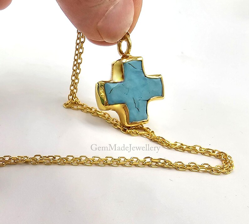 May include: A gold chain necklace with a turquoise cross pendant. The cross is a simple, geometric design with a slightly textured surface.