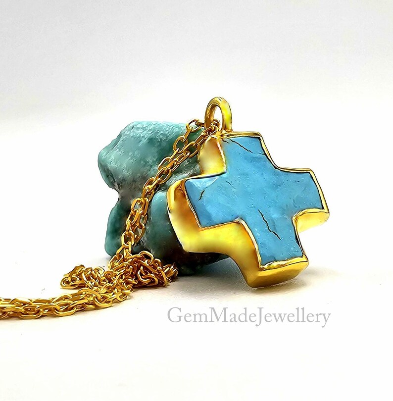 May include: Gold chain necklace with a turquoise cross pendant. The cross is set in gold and has a textured surface.