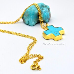May include: A gold chain necklace with a turquoise cross pendant. The cross is made of gold and has a turquoise stone in the center. The necklace is on a white background.