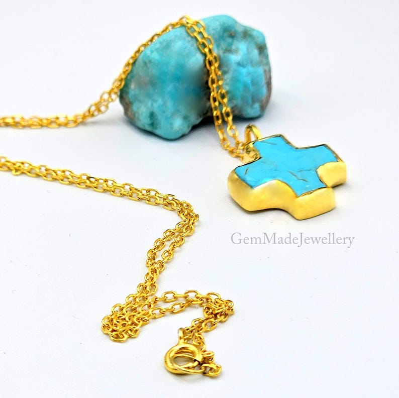 May include: A gold chain necklace with a turquoise cross pendant. The cross is made of gold and has a turquoise stone in the center. The necklace is on a white background.