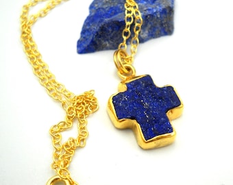May include: Gold chain necklace with a lapis lazuli cross pendant. The cross is made of a natural stone with a deep blue color and gold accents.