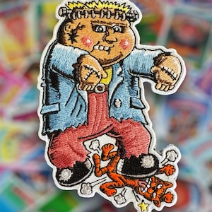 May include: An embroidered iron-on patch featuring a cartoon monster with stitches and a cat underfoot. The monster is wearing a blue jacket, red pants, and black shoes. The cat is orange and has a white star under it.