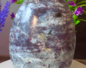 May include: A polished, oval-shaped stone with a marbled appearance. The stone features a mix of gray, white, and deep red-purple hues. The surface has natural cracks and variations in color, giving it a unique, organic look. The stone is a decorative item.